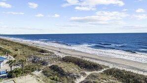 A beach with a sandy shore, a paved walkway, and a grassy area with a fence. - Beautiful Ocean Front 5th Flr Condo (North Myrtle Beach)