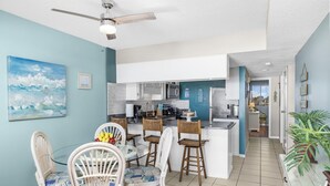 A spacious kitchen with white cabinets, a central island, and a dining area with wicker chairs and a glass table. - Beautiful Ocean Front 5th Flr Condo (North Myrtle Beach)