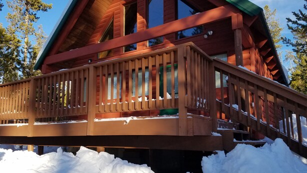 Eine Holzhütte mit einer Veranda und großen Fenstern, umgeben von Schnee.