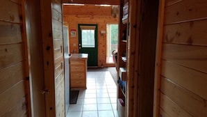 Ein Holzblock-Interieur mit Küchenbereich, einer grünen Tür und Blick ins Freie.