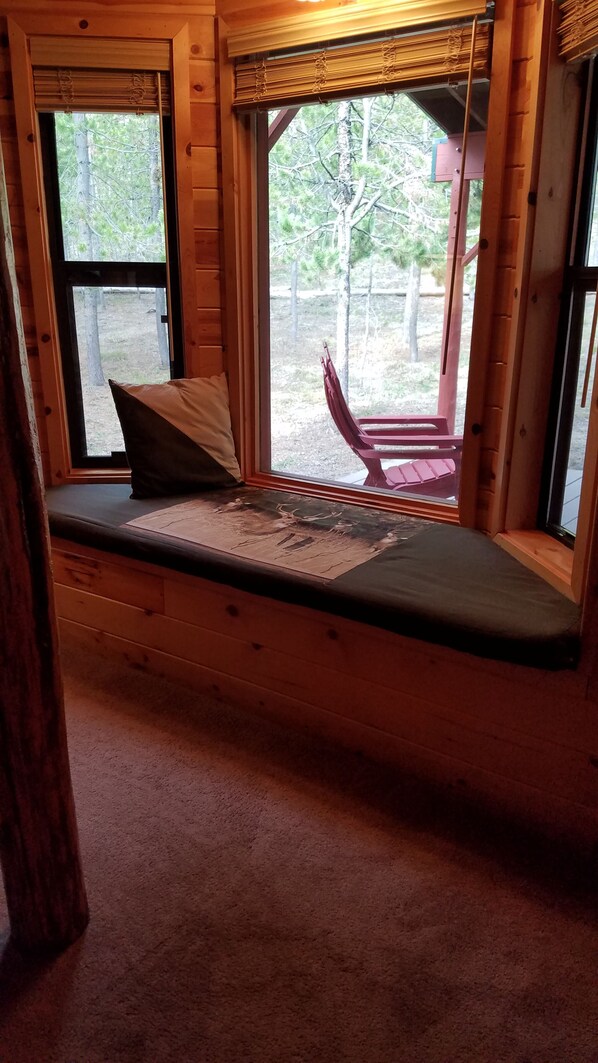 A wooden cabin interior with a bench seat, a pillow, and a view of the outdoors through a window. - Secluded cabin get away! Rest/Relax, fish, boat, hike, bike, ATV, Yellowstone. (Island Park)