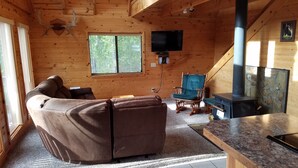 Ein gemütliches Blockhauss-Interieur mit einem braunen Ledersofa, einem Kamin aus Stein und einem an der Wand befestigten Fernseher.