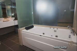 A modern bathroom with a large white bathtub, a glass shower enclosure, and a vanity with a mirror. - Solid Hotels (Masai)
