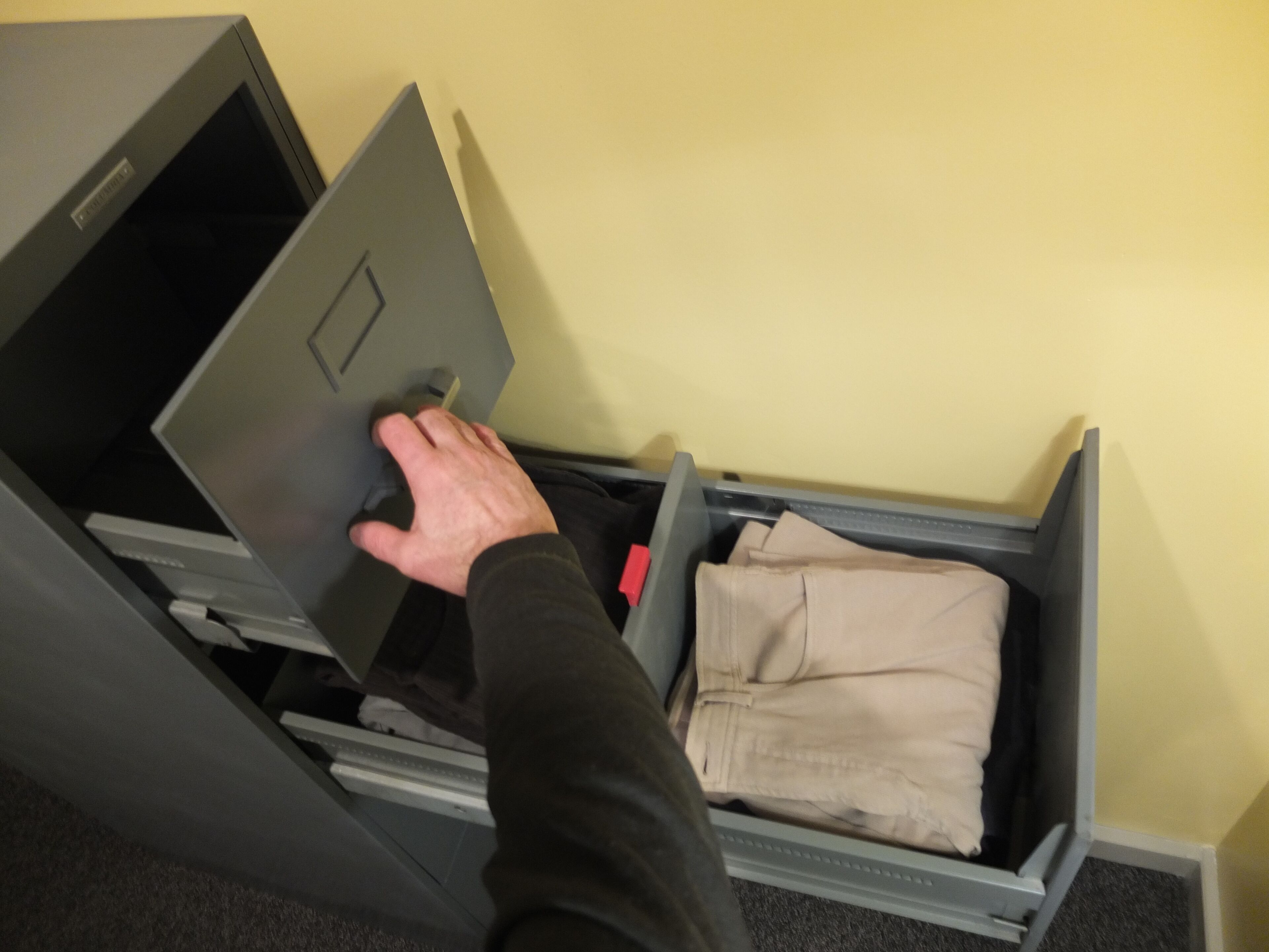 A hand opening a grey filing cabinet drawer with a beige folder inside.