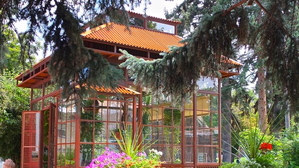 Ein Wintergarten mit Glasfassade, umgeben von Topfpflanzen und Gartenmöbeln.