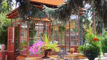 Une véranda avec une structure en verre, entourée de plantes en pot et de meubles d’extérieur.