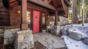 A wooden cabin with a red door, stone walls, and a stone staircase.