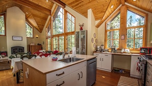 A spacious kitchen with a large island, wooden ceiling, and large windows.
