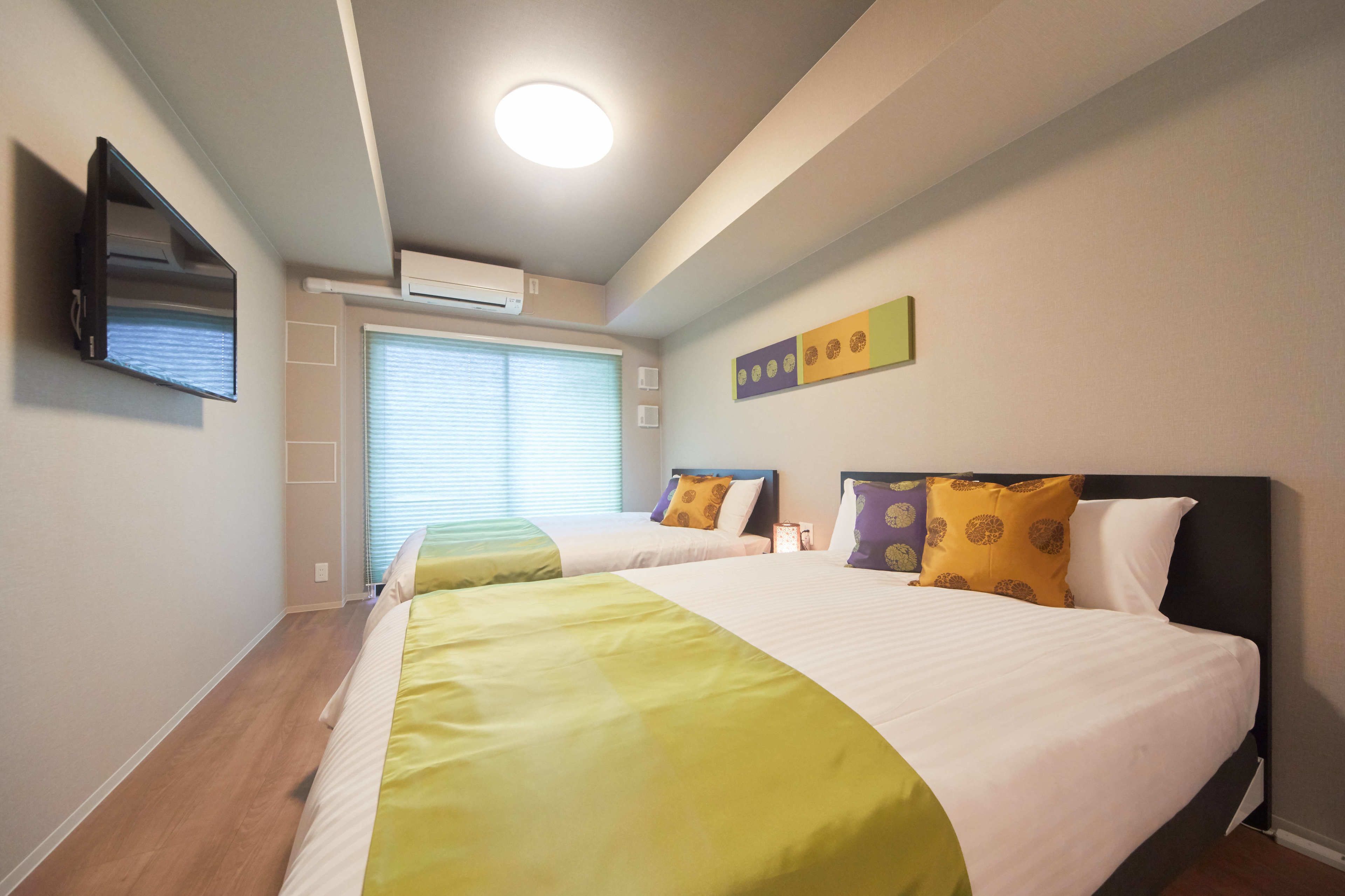 Una habitación de hotel con dos camas, un televisor de pantalla plana, un aire acondicionado y una ventana con persianas.