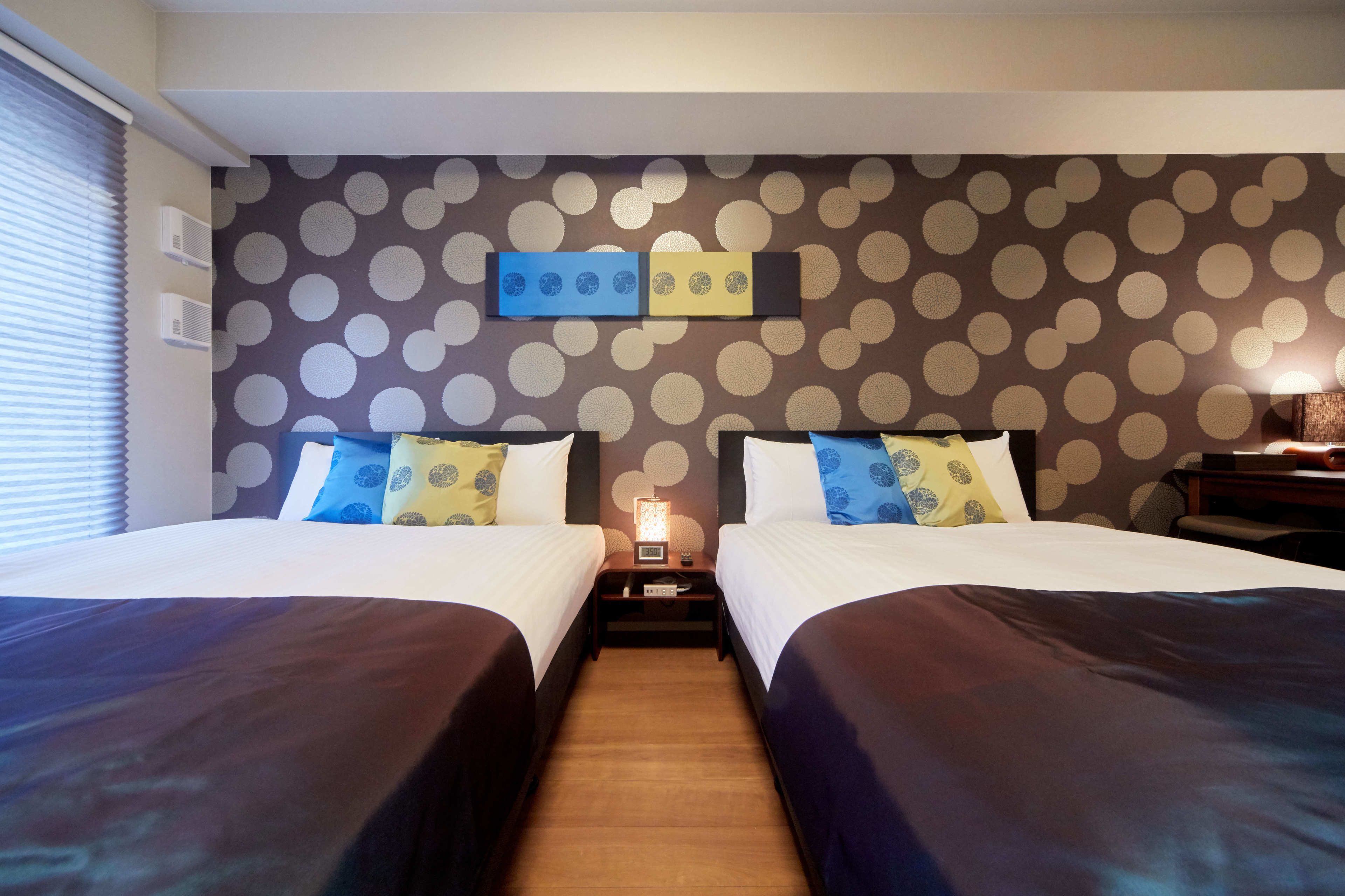 A hotel room with two beds, a wall clock, and a polka dot wallpaper.