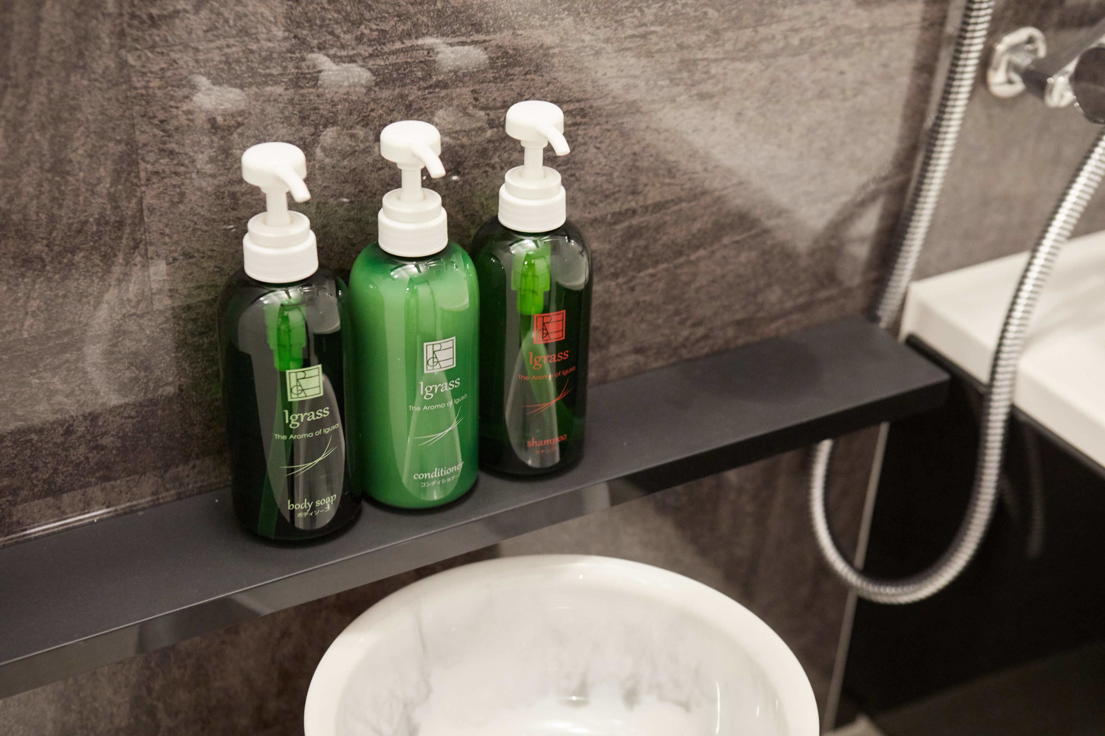 A bathroom shelf with three bottles of body soap and a white sink.