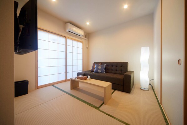 A living room with tatami flooring, a sofa, a coffee table, and a traditional Japanese shoji screen door.