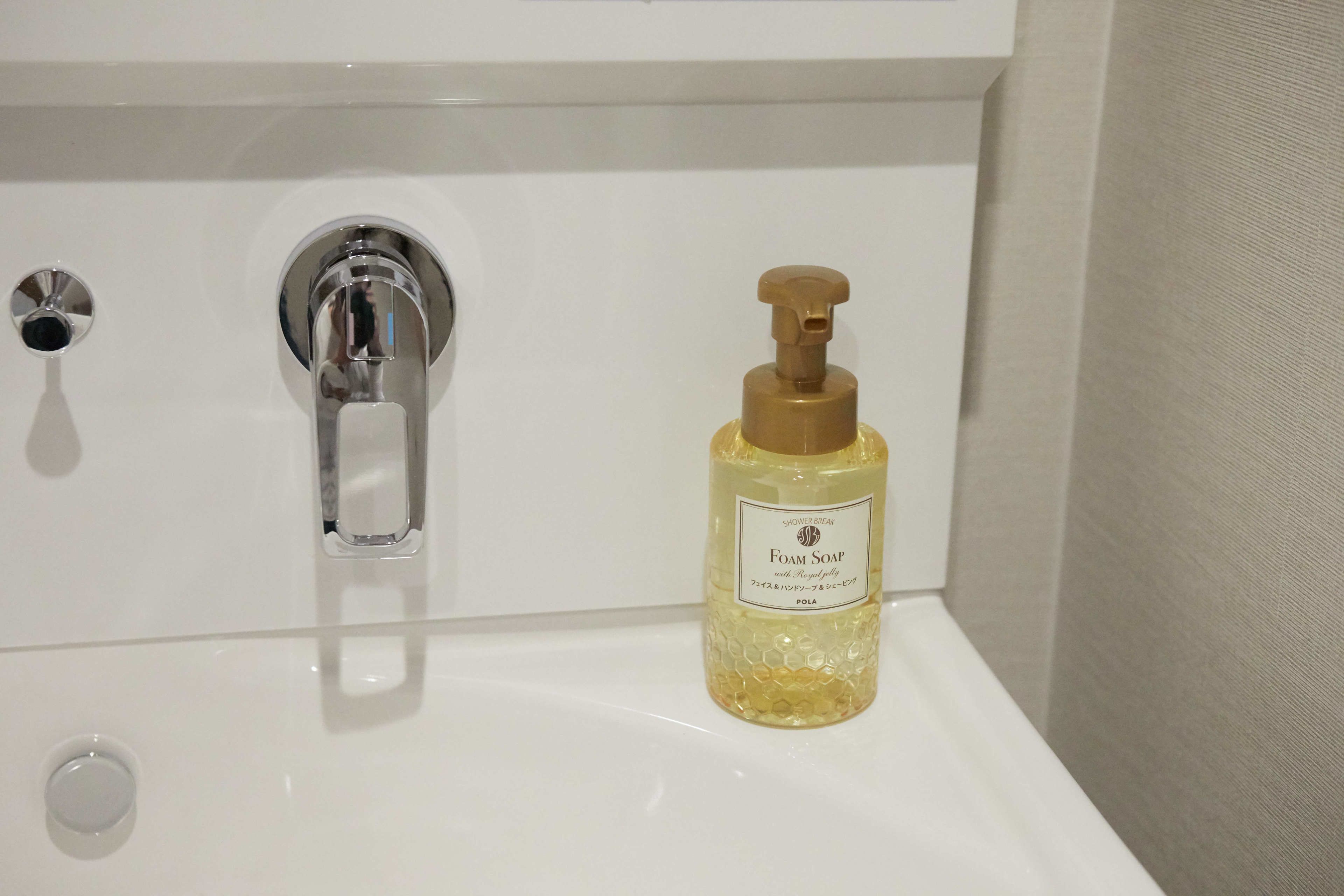 A bathroom sink with a chrome faucet and a bottle of foam soap.