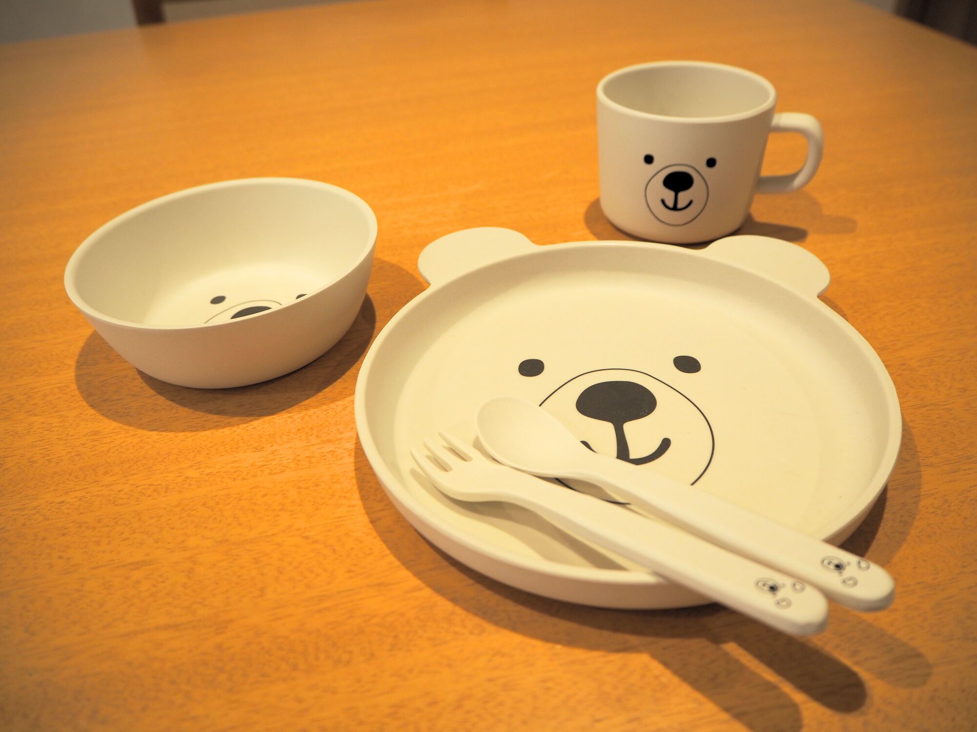 A wooden table with a white bear-themed plate, a white bowl, and a white mug.