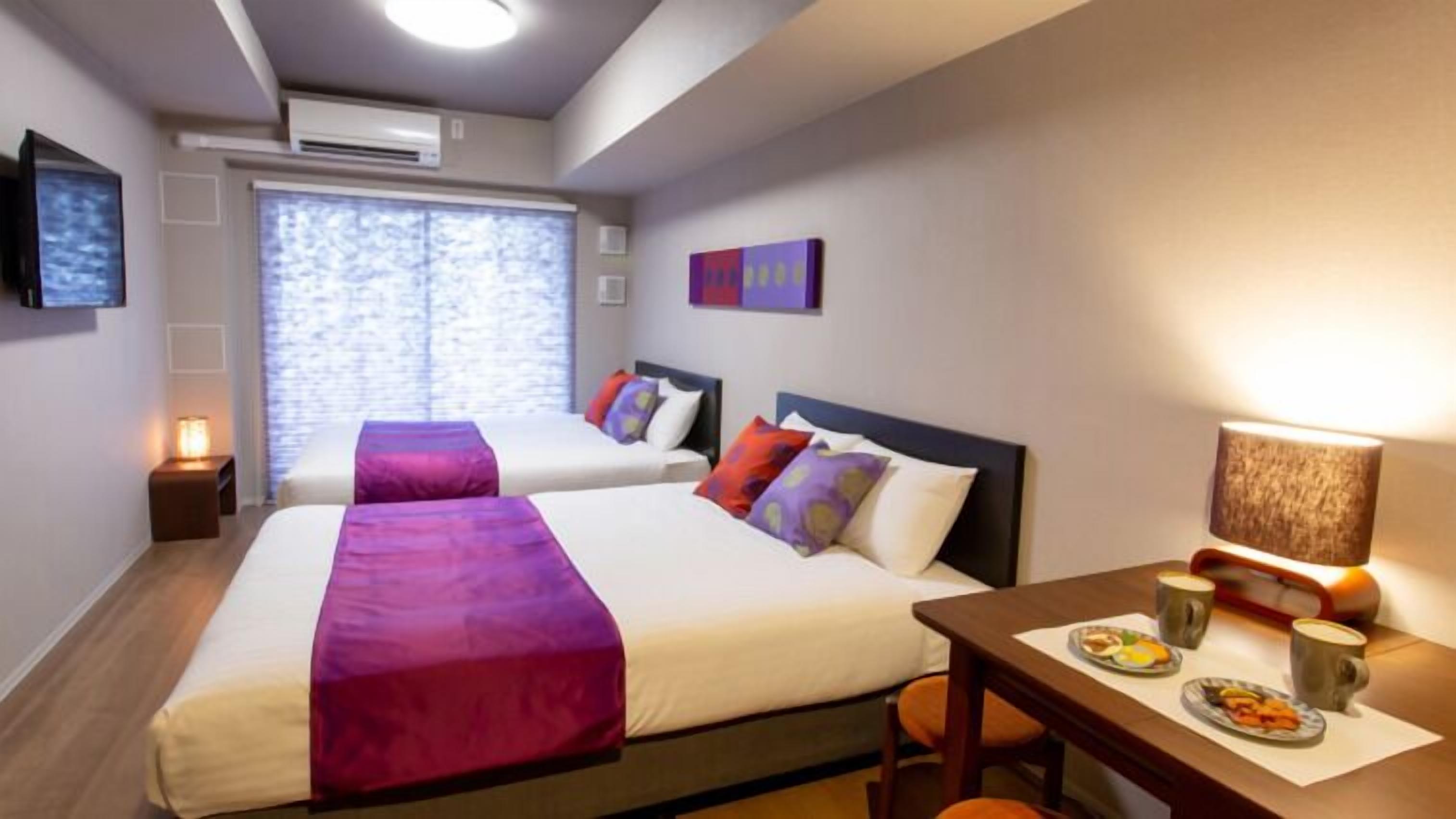 A hotel room with two beds, a dining table with breakfast, and a TV on the wall.