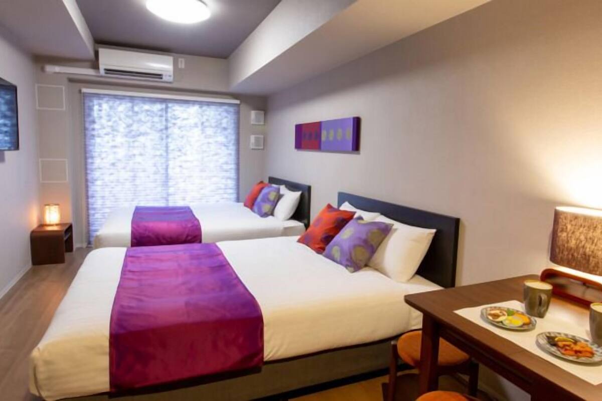 A hotel room with two beds, a dining table with breakfast, and a TV on the wall.