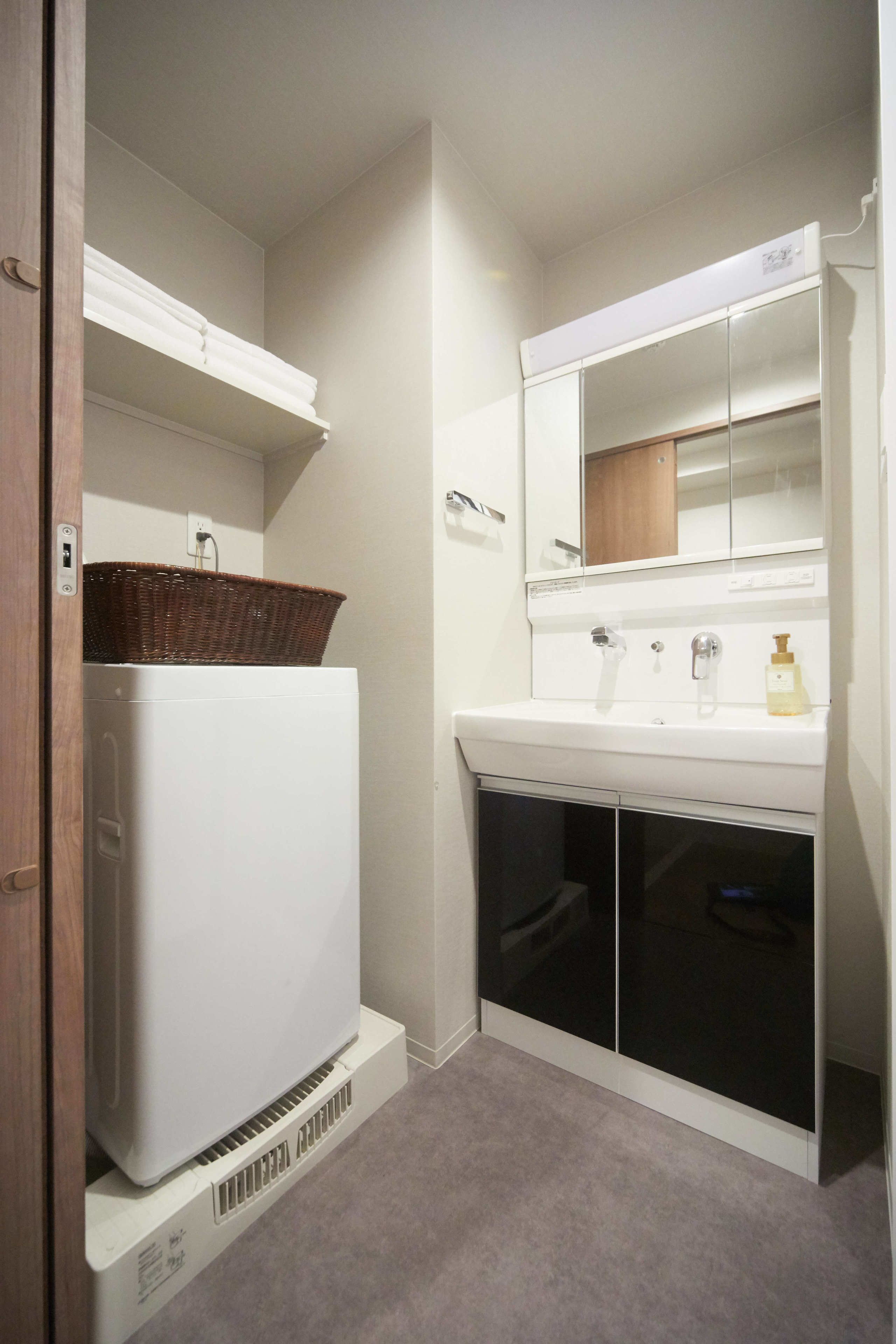 A compact bathroom with a white sink, mirror, and a white appliance, possibly a washer or dryer, with a basket on top.