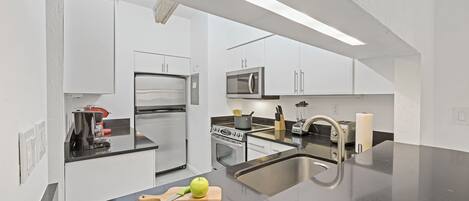 A modern kitchen with white cabinetry, stainless steel appliances, and a black countertop.