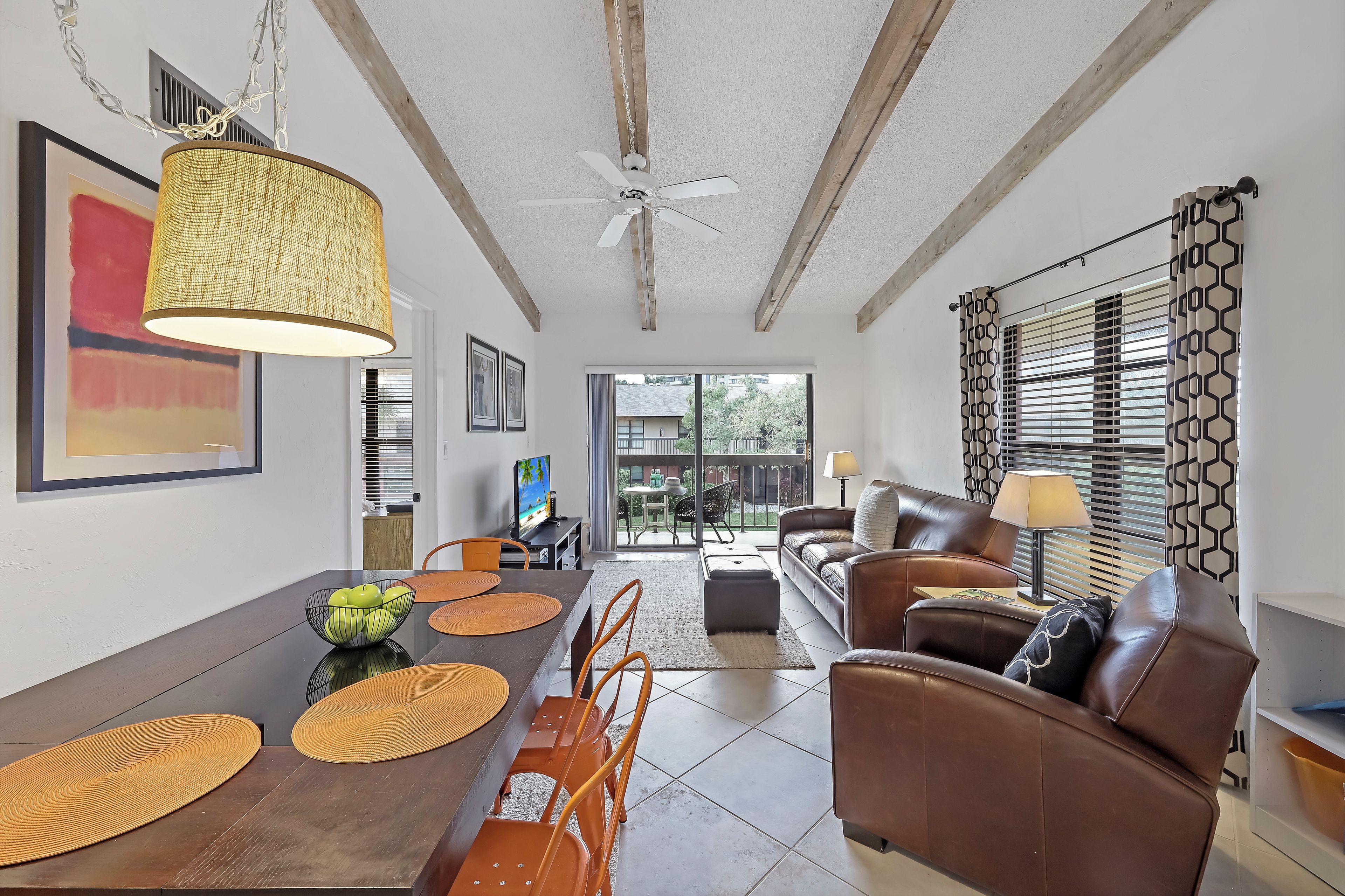 A spacious living area with a dining table, brown leather sofa, and a ceiling fan.