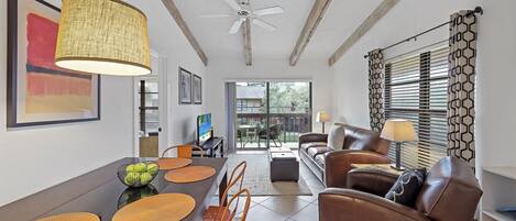 A spacious living area with a dining table, brown leather sofa, and a ceiling fan.