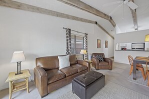 A modern living room with a brown leather sofa, a matching ottoman, a wooden side table, and a dining area with a wooden table and chairs. - Inviting Condo | Pool Just Steps From The Beach (Marco Island)