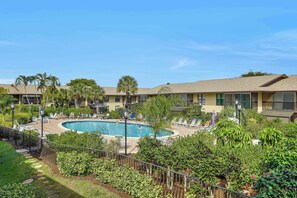 A hotel with a swimming pool surrounded by lounge chairs and palm trees.