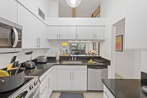 A modern kitchen with white cabinets, a black countertop, a built-in microwave, and a stove.