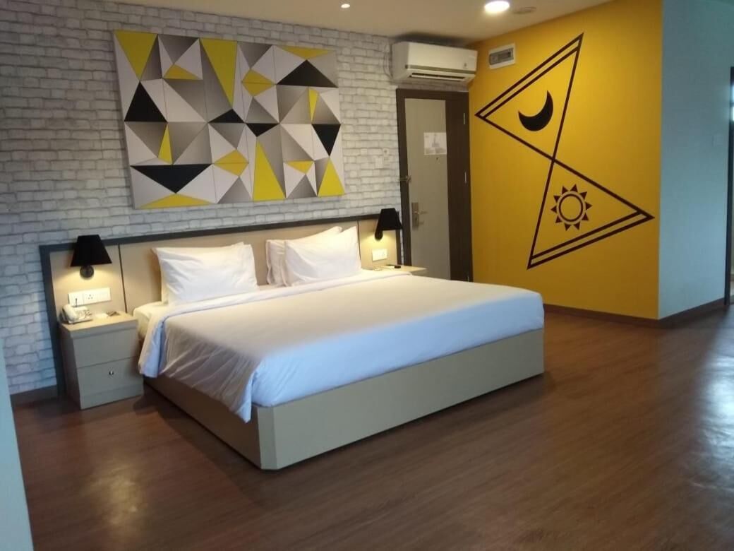 A modern hotel room with a large bed, a nightstand, a wall-mounted air conditioner, and a geometric wall decoration.