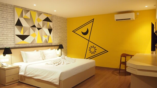 A hotel room with a bed, nightstands, a desk, and a chair. There is a geometric wall art piece above the bed and a wall-mounted air conditioner. - Nite & Day Laguna Bintan - Tanjungpinang (Tanjung Pinang)