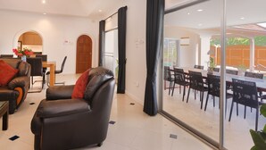 Uma sala de estar moderna com sofás de couro, uma área de jantar com cadeiras pretas e uma grande porta de vidro que dá para um pátio externo.
