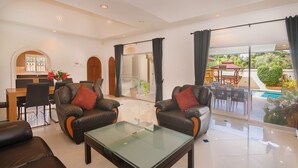 Ampla sala de estar com sofás de couro, uma mesa de centro de vidro e uma área de jantar com mesa e cadeiras de madeira.