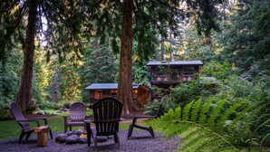 A cabin surrounded by a forest with outdoor seating and a view of the cabin.