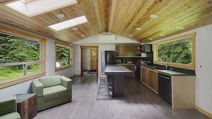A modern kitchen with wooden beams, large windows, and a green sofa.