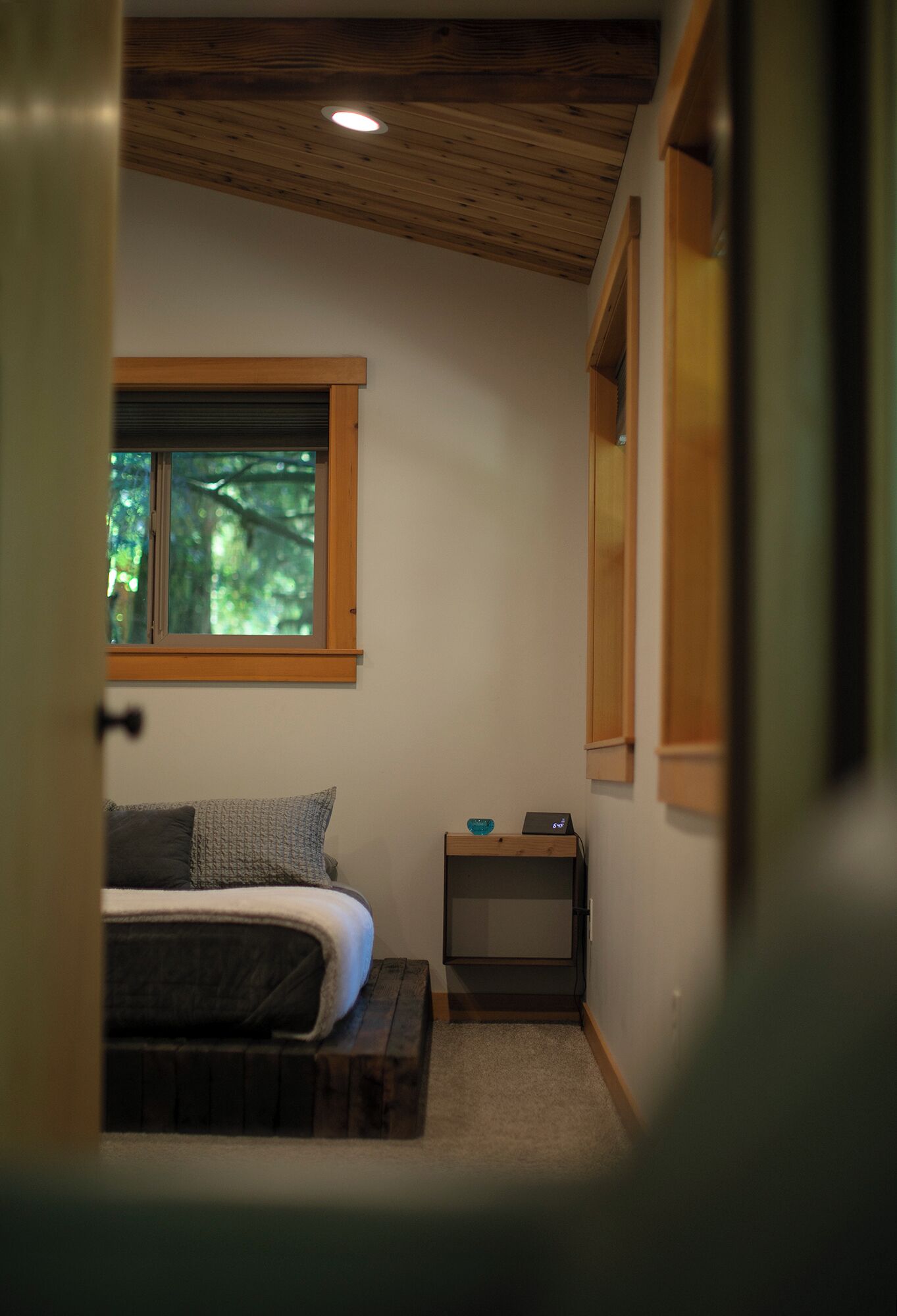 Un dormitorio con cama, mesita de noche, ventana y techo de madera.