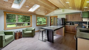 A modern kitchen with a central island, large windows, and a cozy seating area with a sofa and chairs.