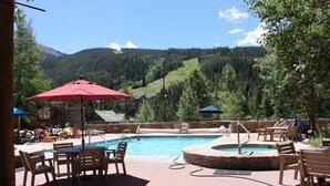 Ein Poolbereich mit Liegestühlen und Sonnenschirmen, eingebettet in eine gebirgige Landschaft.