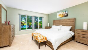 Un dormitorio con una cama grande, una mesita de noche de madera, un aparador y una ventana con vistas a la vegetación.