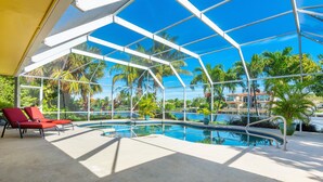 Piscina al aire libre techada con sillas reclinables rojas, rodeada de palmeras y un cielo azul despejado.