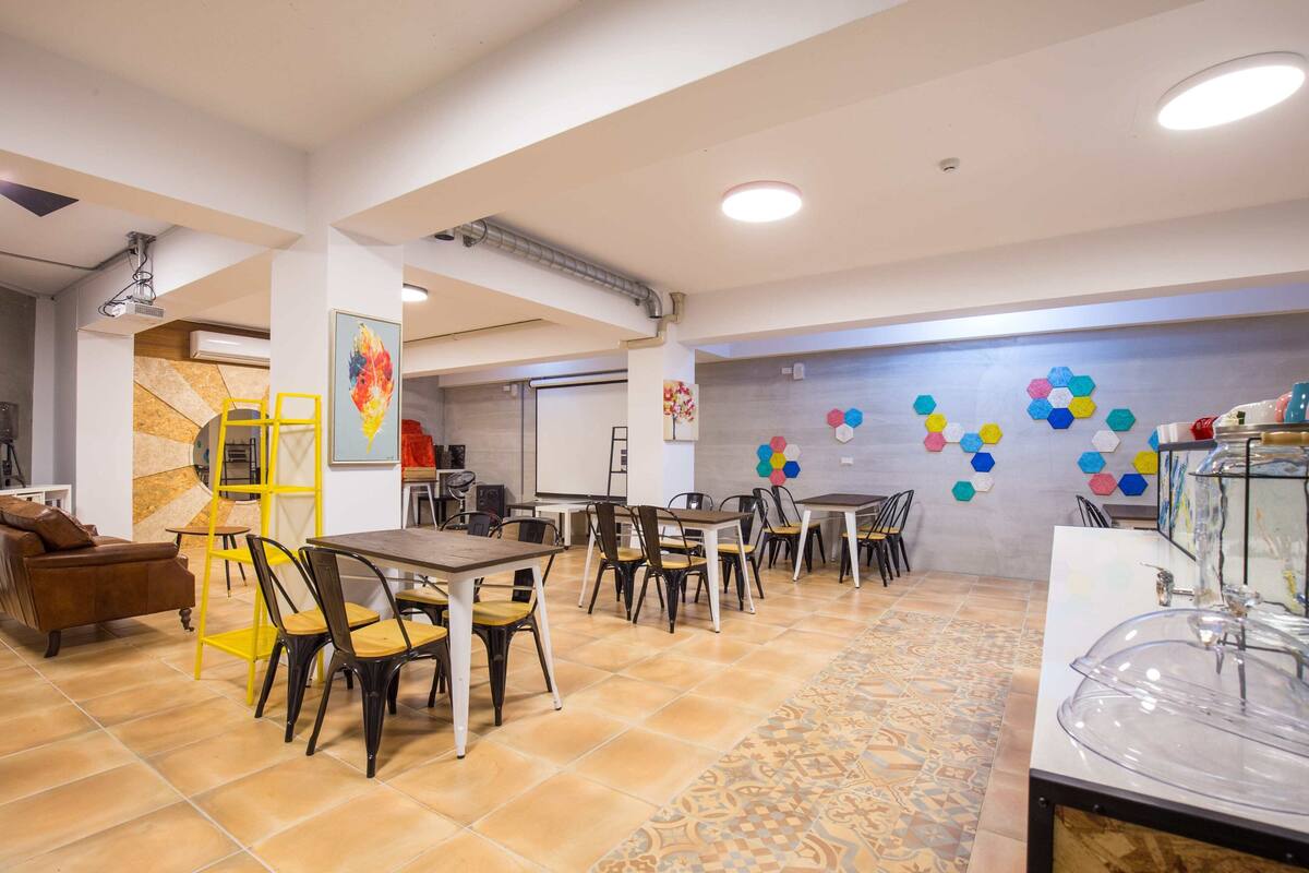 A dining area with multiple tables and chairs, a yellow ladder, and a decorative wall with hexagonal patterns.
