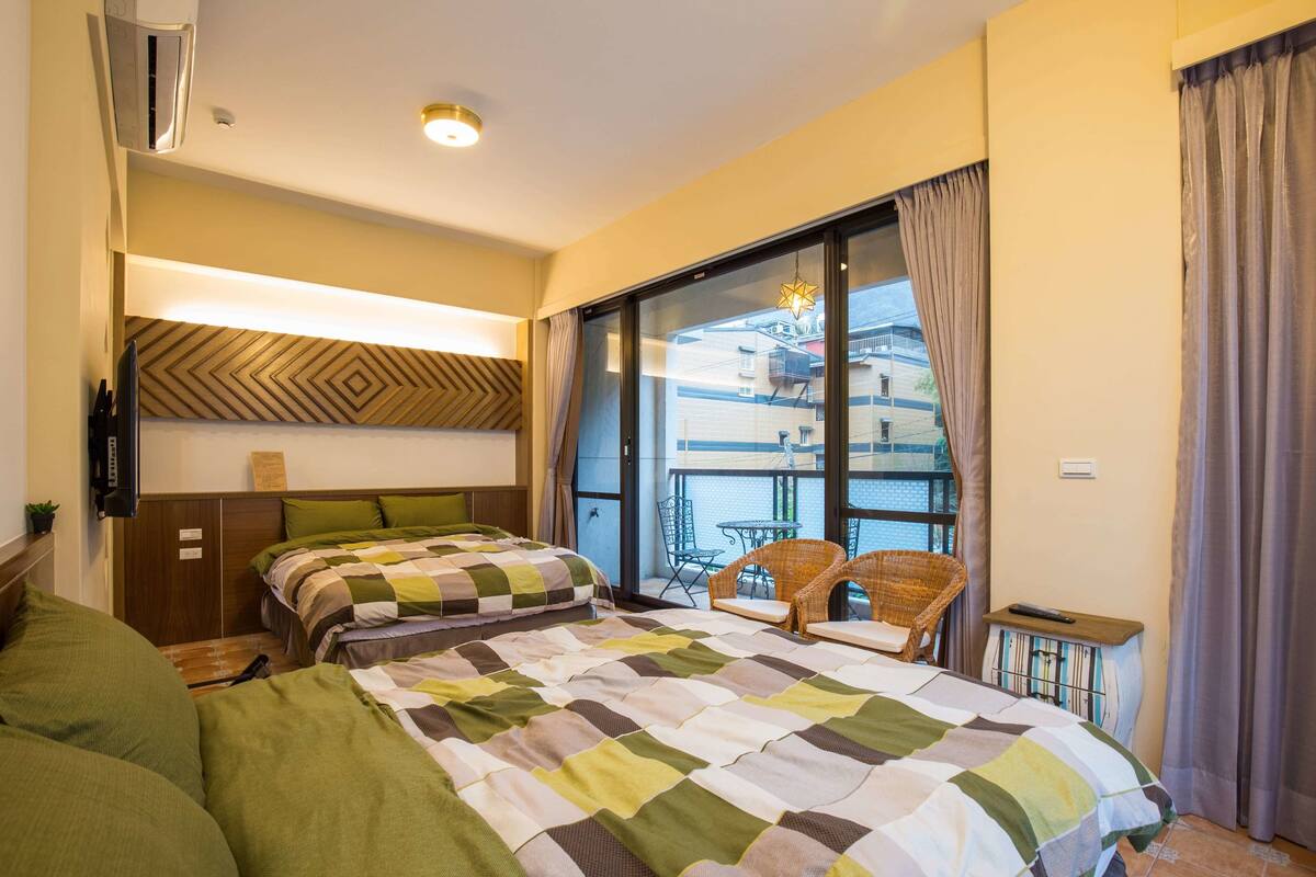 A hotel room with two beds, a balcony with a view, a small table, and a chair.