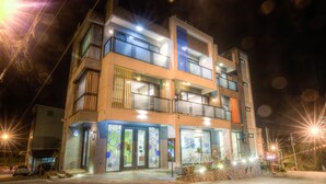 A multi-story hotel with balconies, a ground-level entrance, and a well-lit facade. - A walk in the mist (Lugu)