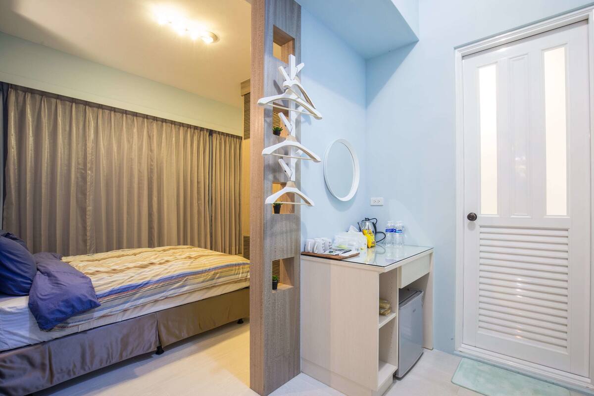 A bedroom with a bed, a desk, a mirror, and a door.