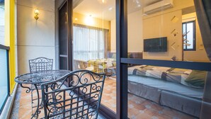 A balcony with a wrought iron table and chairs, a bed with a patterned bedspread, and a television in the room. - A walk in the mist (Lugu)