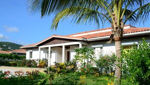Um edifício branco com telhado de telhas vermelhas, rodeado por vegetação exuberante e plantas floridas.