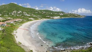Uma área costeira com praia, águas azul-claras e um morro com edifícios.