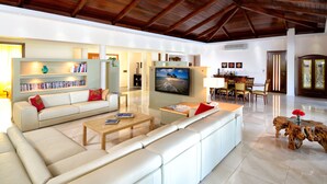 Uma sala de estar ampla com pé direito alto, um sofá, uma mesa de centro, uma TV e um espaço de jantar com cadeiras e mesa.