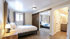 A bedroom with a bed, bedside table, lamp, and a view of another room through a door. - Shepherd Family Retreat- Fox | Main Home & Guest House sleeps 12 Near Yellowstone (West Yellowstone)