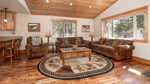 A cozy living room with wooden flooring, a round coffee table, two sofas, and a dining area with wooden chairs. - Shepherd Family Retreat- Fox | Main Home & Guest House sleeps 12 Near Yellowstone (West Yellowstone)