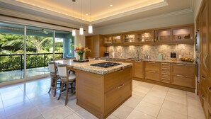A modern kitchen with a large island, wooden cabinets, and a view of lush greenery. - HO'OLEI #24-3-BEAUTIFULLY APPOINTED VILLA-SLEEPS 10-METICULOUS CLEANING (Wailea)