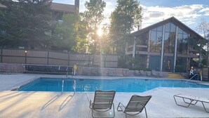 A swimming pool with lounge chairs, a stone wall, and a building with large windows in the background. - A Wasatch Wonderland  Beautiful 2 + 2, Dog Friendly (Park City)